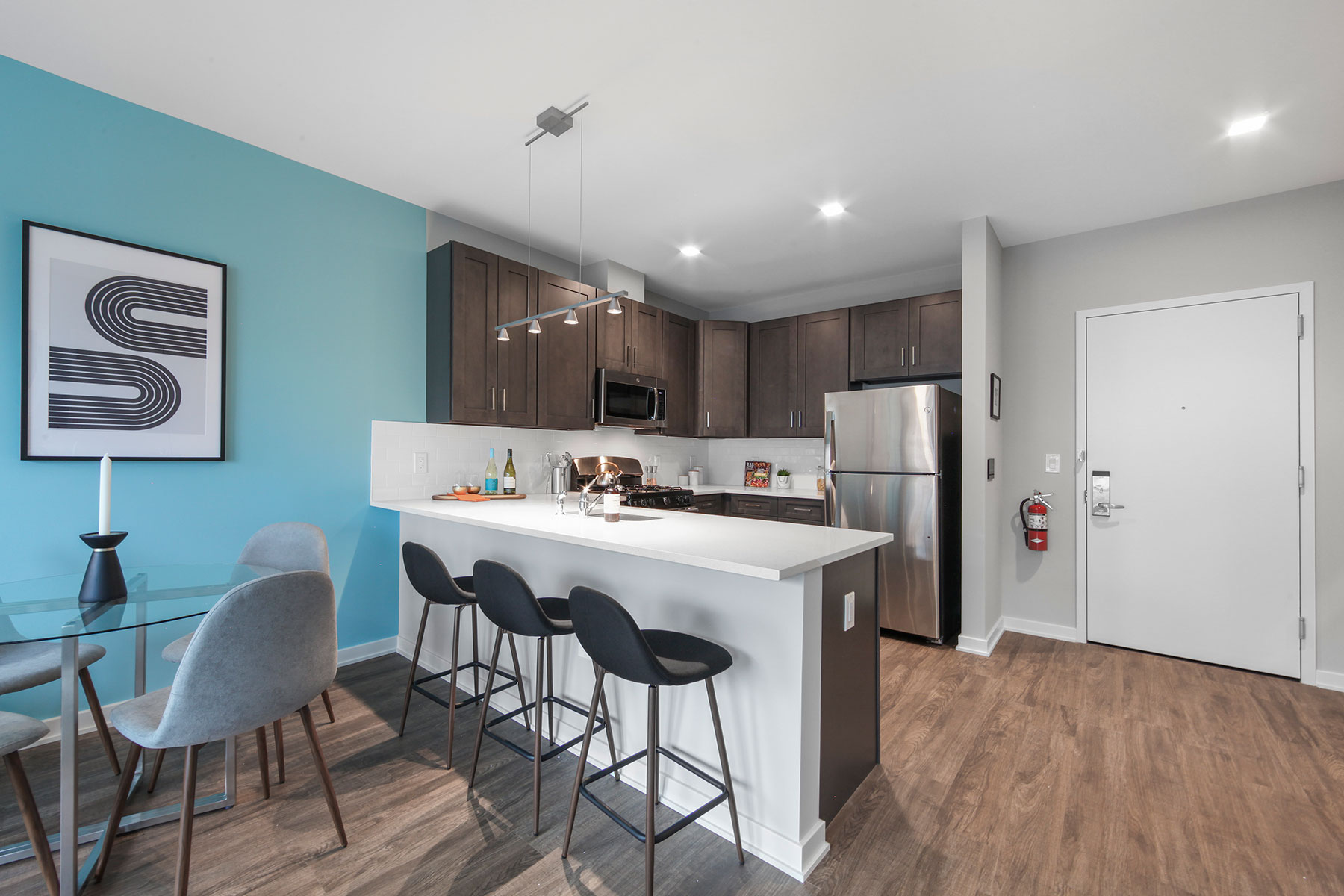 Bright modern kitchen and dine in seating near entrance, with barstools at counter, dark wood cabinetry, stainless steel appliances and modern fixtures and wood floors